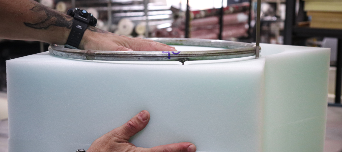 Profissional medindo e cortando espuma sob medida em bloco, mostrando o processo de produção em fábrica — ideal para quem procura onde comprar espuma por metro.