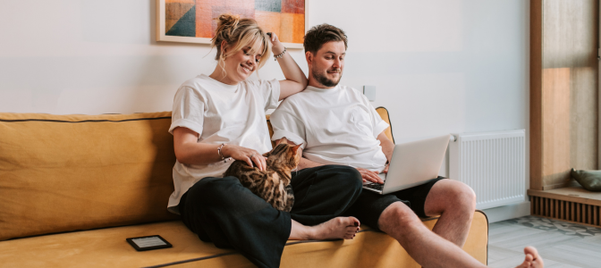 Casal relaxando em um sofá amarelo enquanto usa notebook, com gato no colo, representando conforto e resistência do estofado.